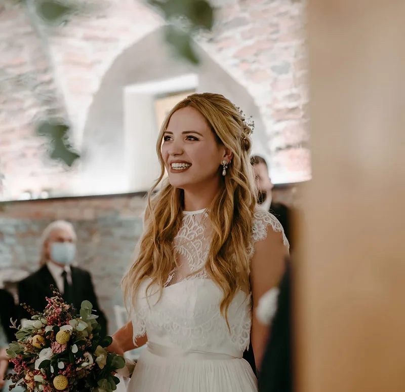 Ritratto di sposa durante la cerimonia: abito da sposa in pizzo e gonna plissettata, con bouquet