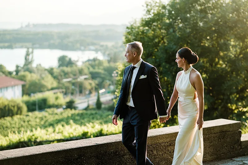 Sposi camminano su una terrazza panoramica al tramonto: abito da sposa minimal con collo all’americana