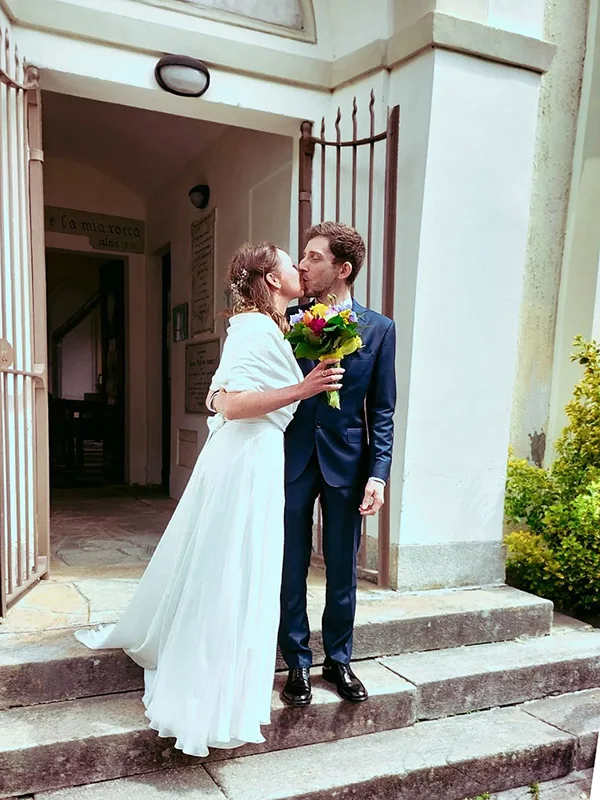 Sposi si baciano sui gradini della chiesa: abito da sposa semplice con mantella