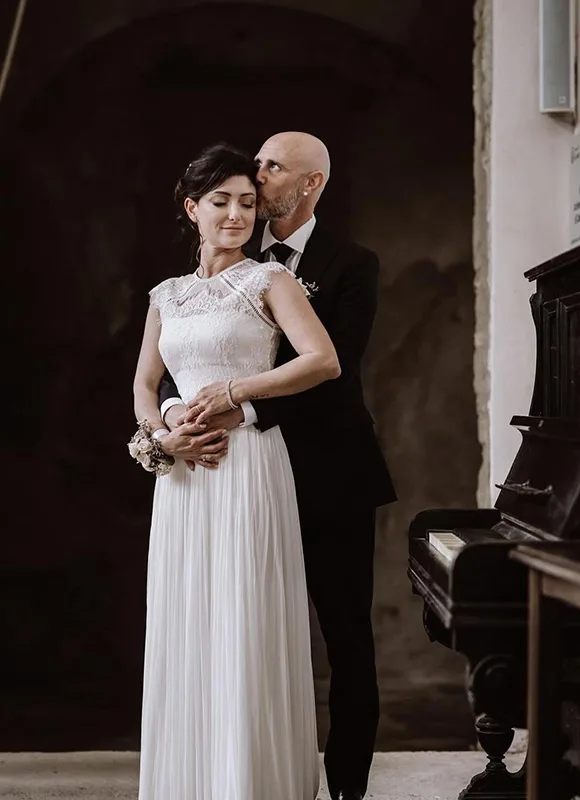 Sposi accanto a un pianoforte: abito da sposa in pizzo e gonna plissettata